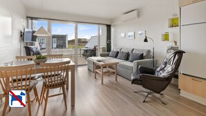 A modern living room with a dining area, a sofa, a leather chair, and a kitchen area with a refrigerator. - Agger Holidays (Vestervig)