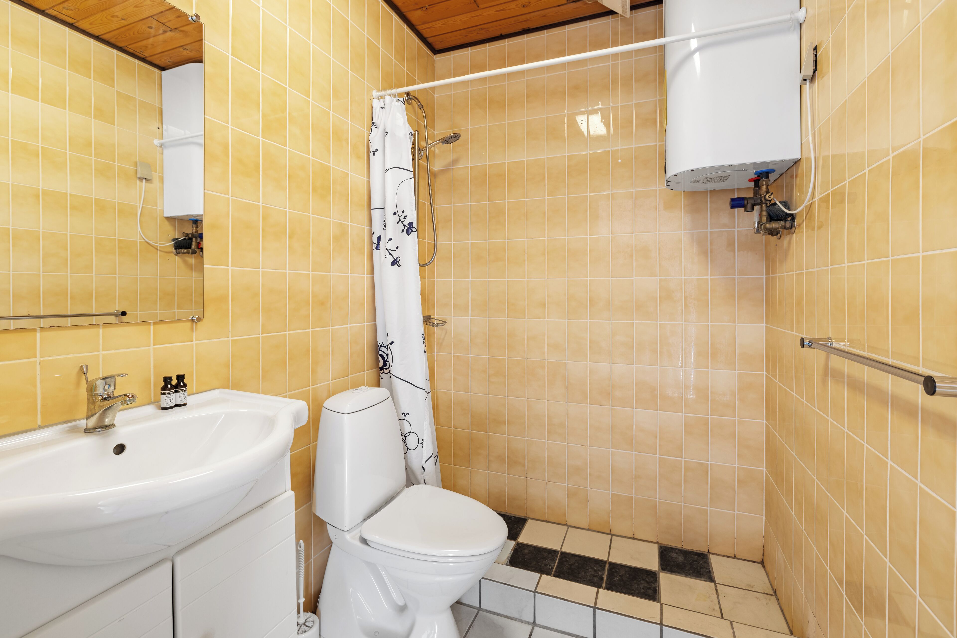 A bathroom with a sink, toilet, shower, and tiled walls.