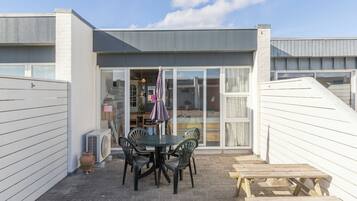 Un espace patio aménagé avec une table et des chaises, un banc en bois et une grande porte-fenêtre coulissante donnant sur un espace intérieur.
