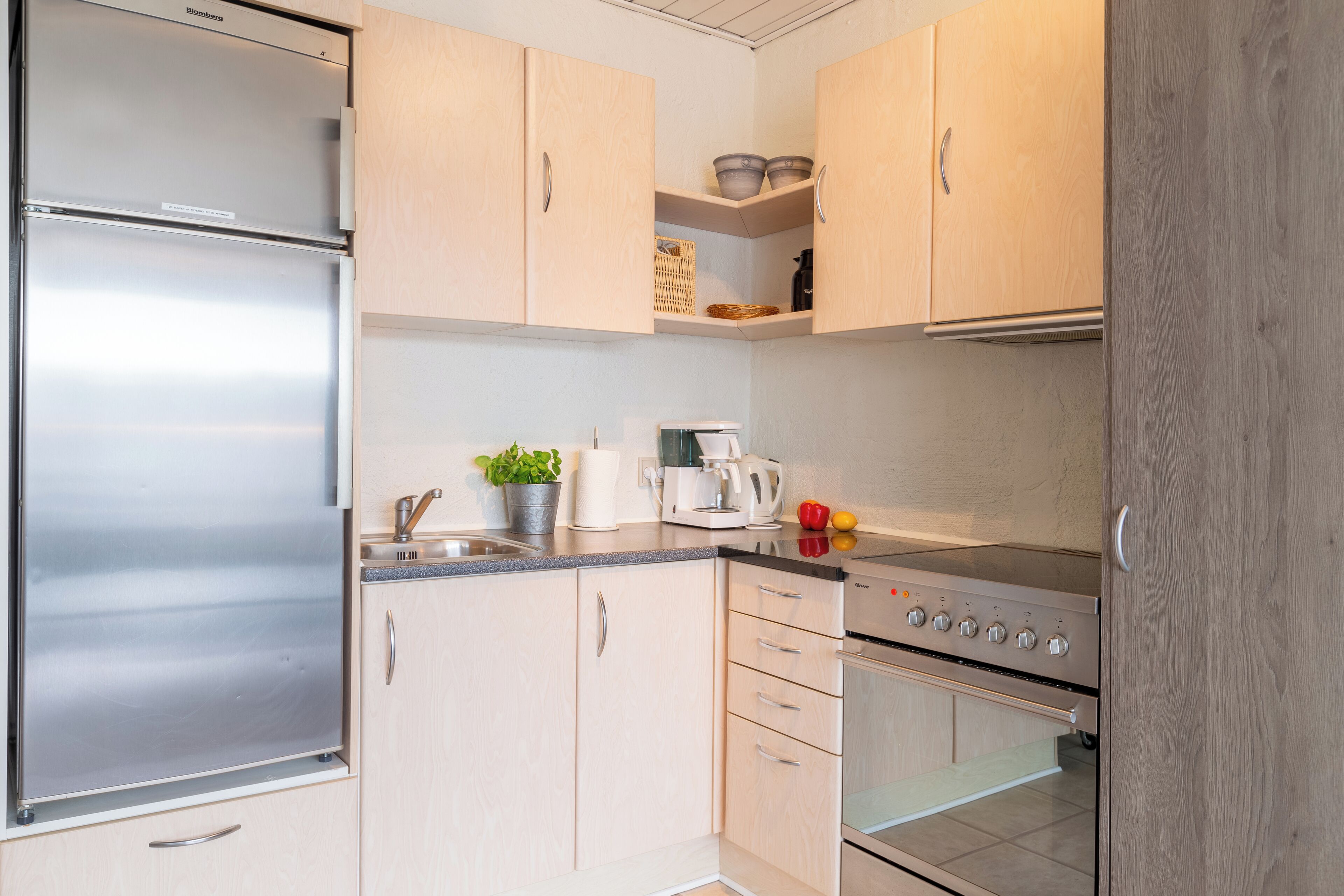 Una cocina moderna con armarios de madera clara, electrodomésticos de acero inoxidable y un horno empotrado.