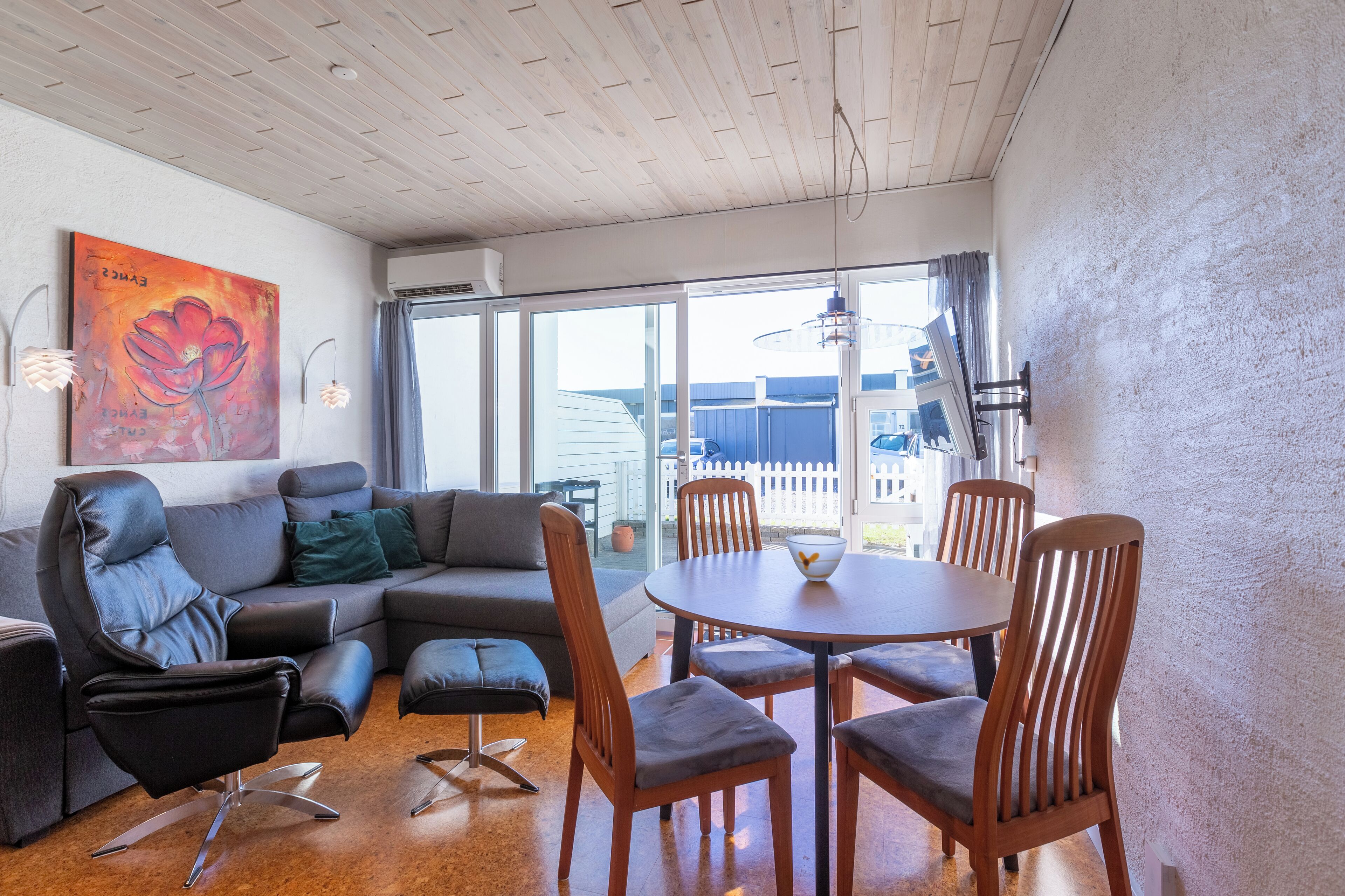 Ein modernes Wohnzimmer mit grauem Sofa, schwarzem Sessel und einem Holzesstisch mit Stühlen.