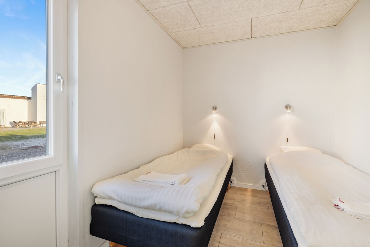 Ein Zimmer mit zwei Betten, einem Fenster und Blick ins Freie.