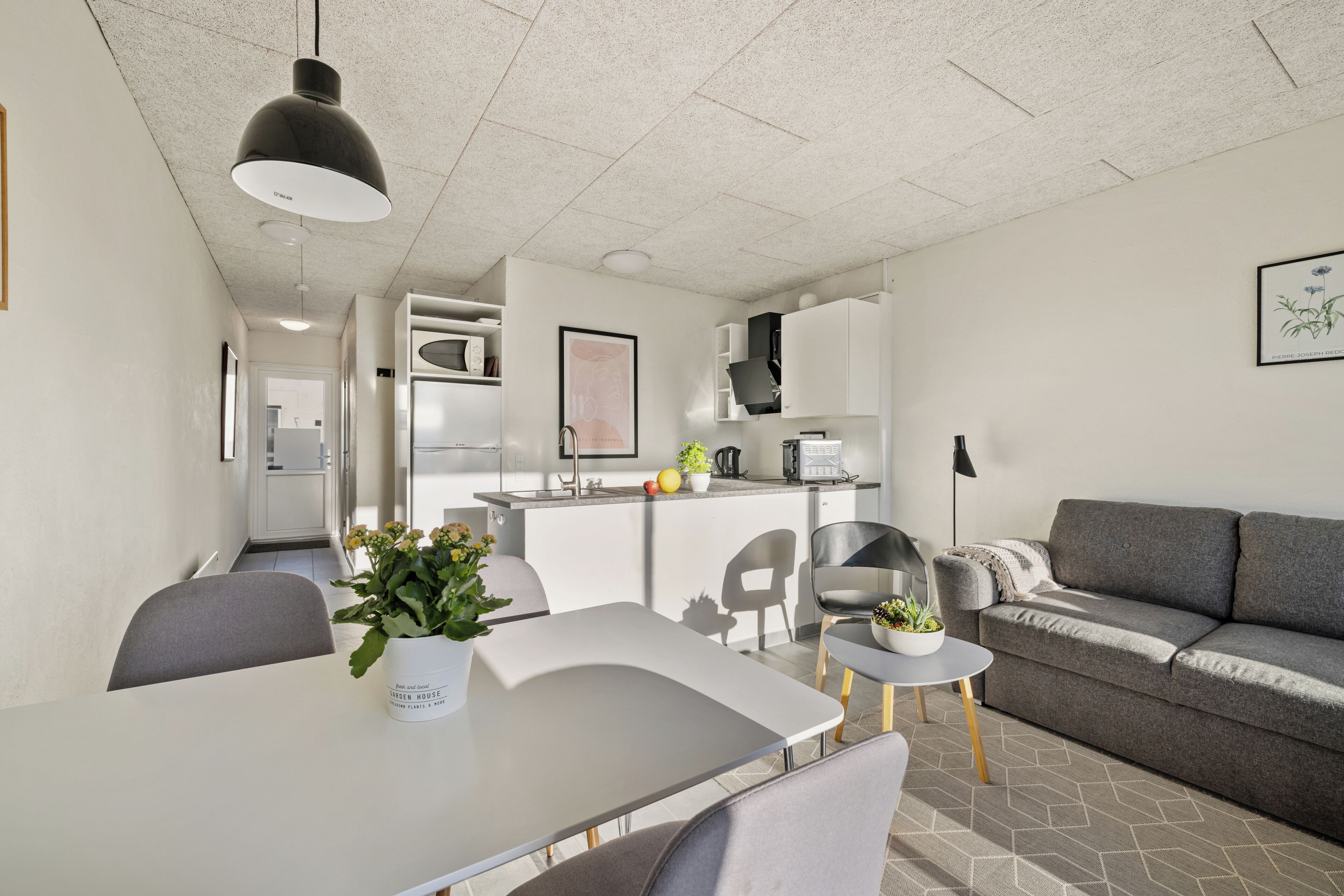 A modern kitchen with white cabinets, a dining table with chairs, and a grey sofa.