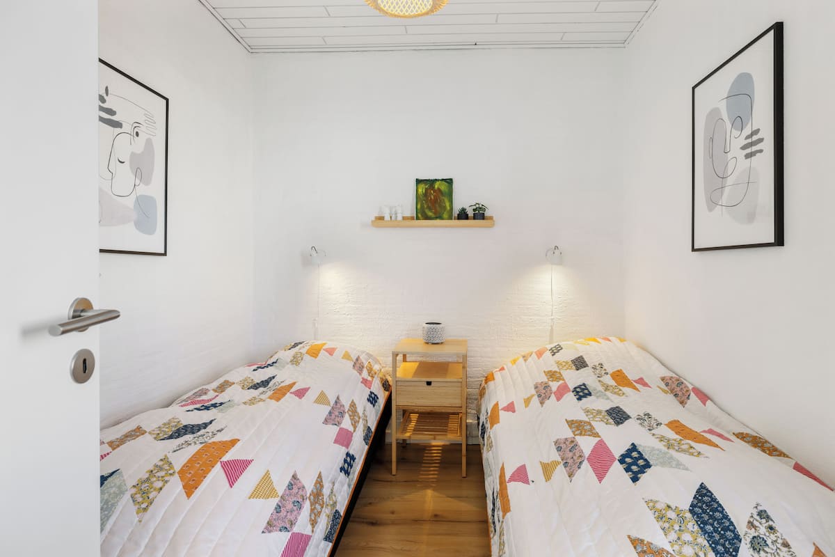 Ein Zimmer mit zwei Betten, einem kleinen Tisch und einem Regal mit Dekoration.