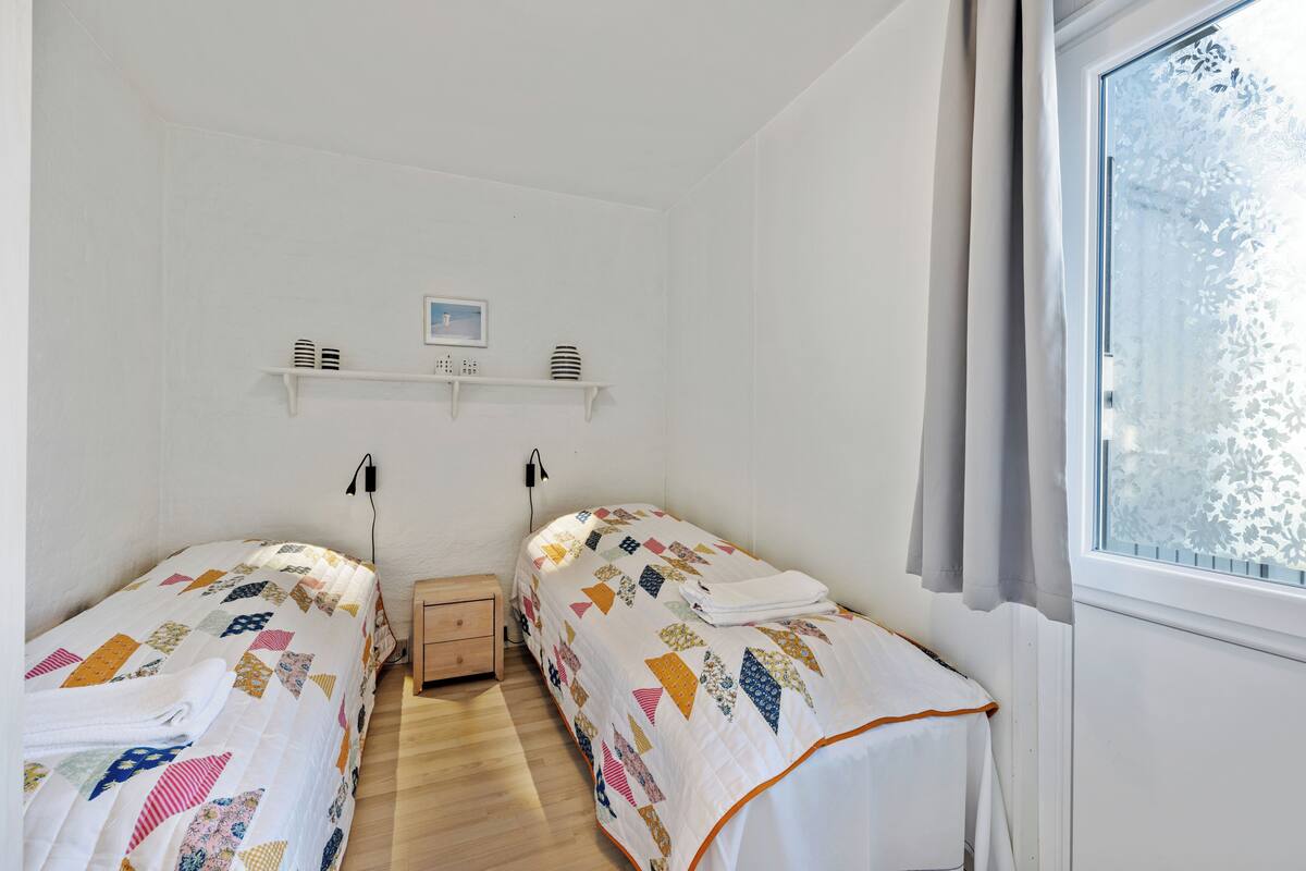 Ein Schlafzimmer mit zwei Einzelbetten, einem kleinen Nachttisch, einem Regal mit Dekoration und einem Fenster mit Vorhängen.