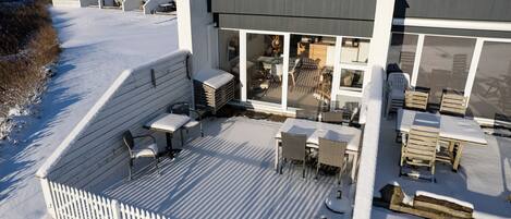 A modern building with a covered outdoor area featuring tables and chairs, a white picket fence, and a view of the surrounding landscape.