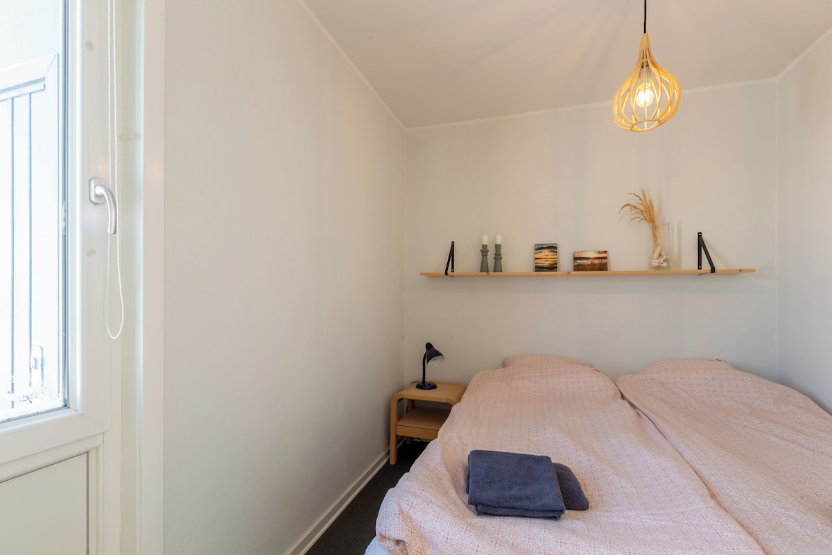 Ein Schlafzimmer mit einem Bett, einem Nachttisch, einer Ablage mit Dekoration und einer Hängeleuchte.