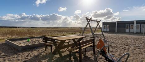 Ein Sandbereich im Freien mit Picknicktischen und einem Spielplatz.
