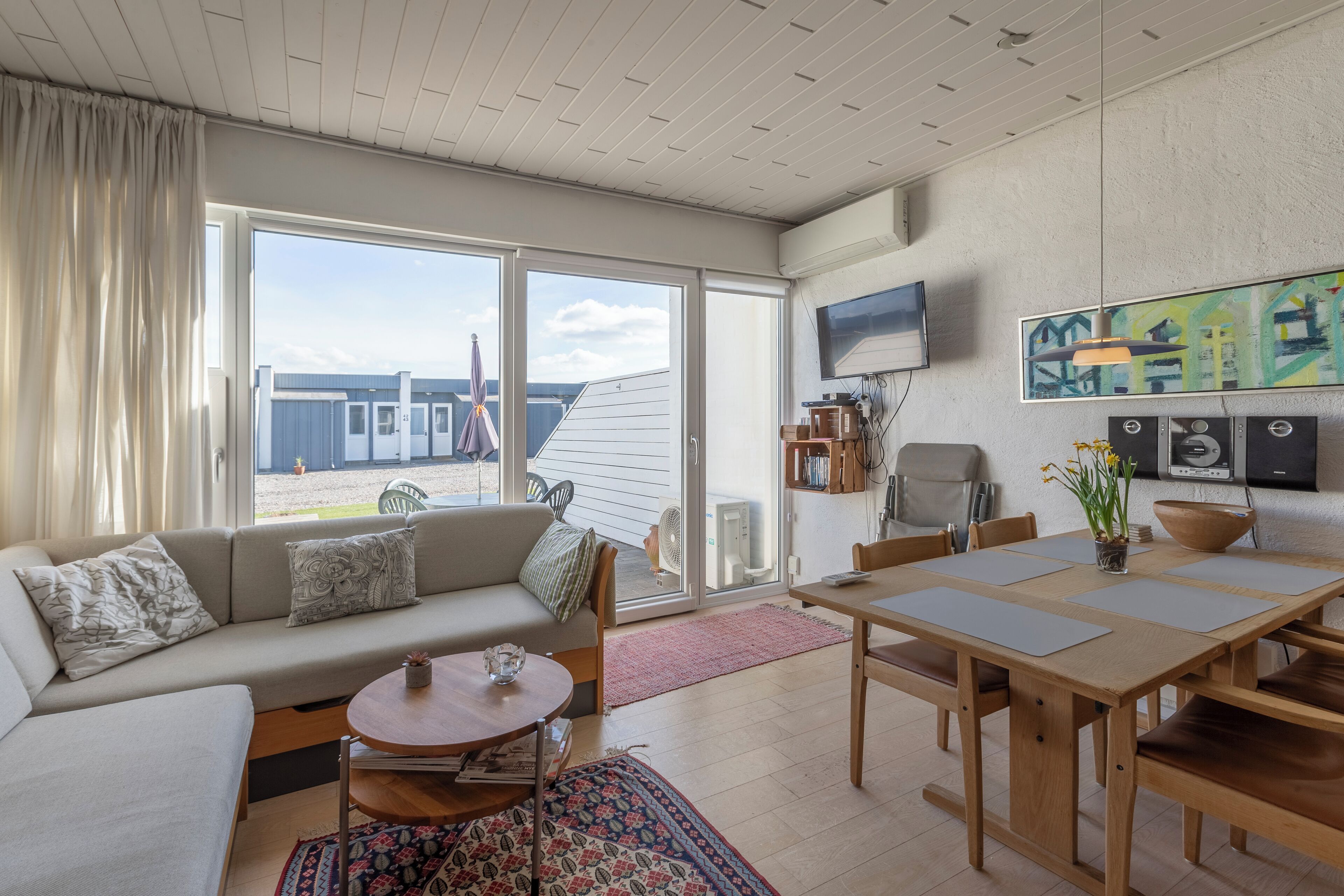 Un salon moderne avec un canapé, une table basse et une table à manger. Une porte-fenêtre coulissante donne accès à un espace extérieur.