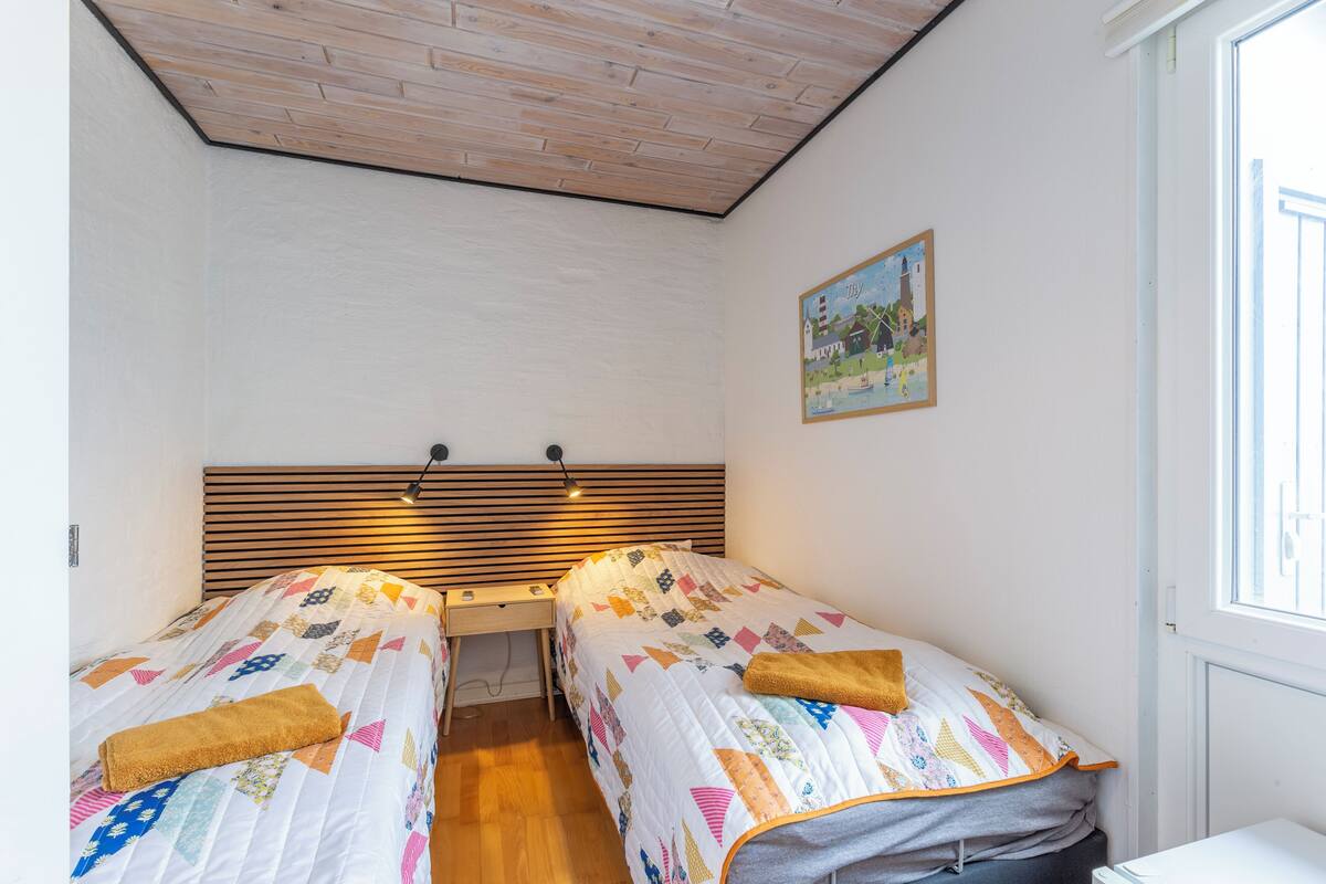 Ein Schlafzimmer mit zwei Einzelbetten, einem Holzkopfteil, Nachttischen, einem Bild an der Wand und einem Fenster.