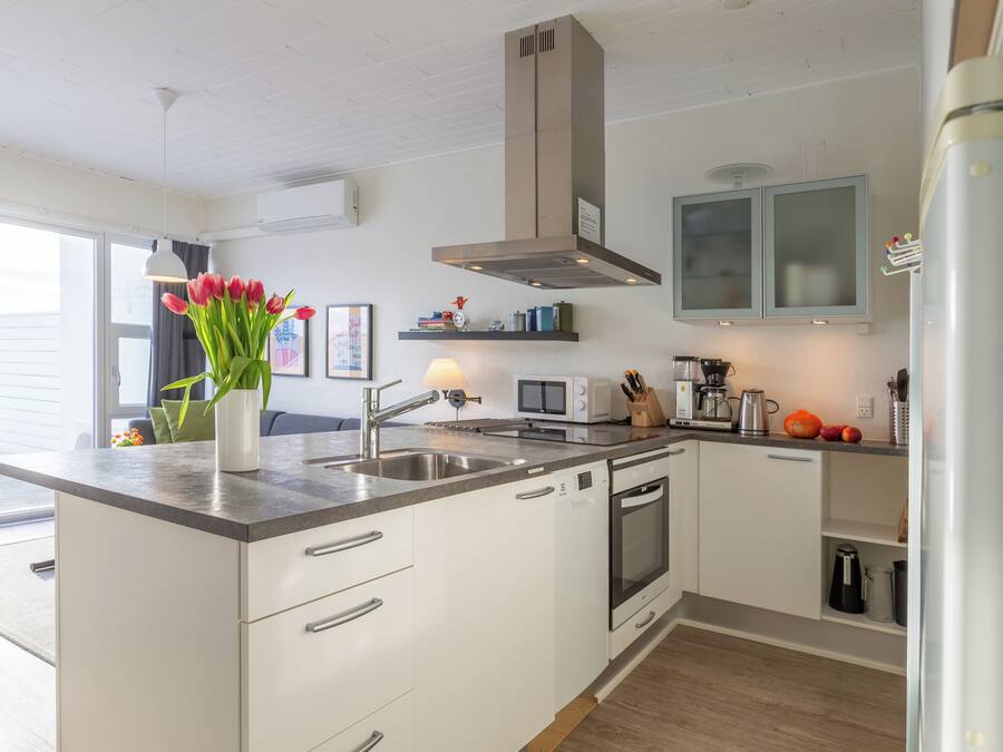 A modern kitchen with white cabinets, a stainless steel sink, and a built-in oven. There is a vase with red flowers on the counter, and a microwave above the sink.