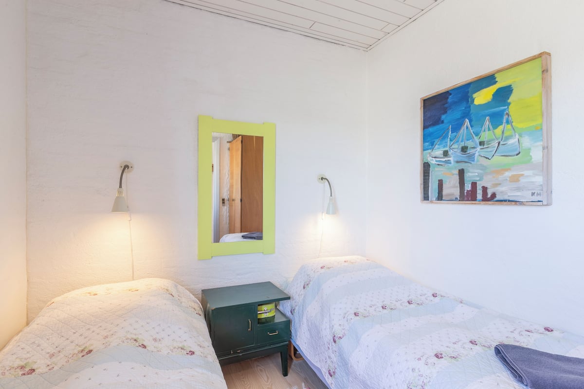 Ein Schlafzimmer mit zwei Betten, einer grünen Kommode, einem Spiegel und einem Bild an der Wand.