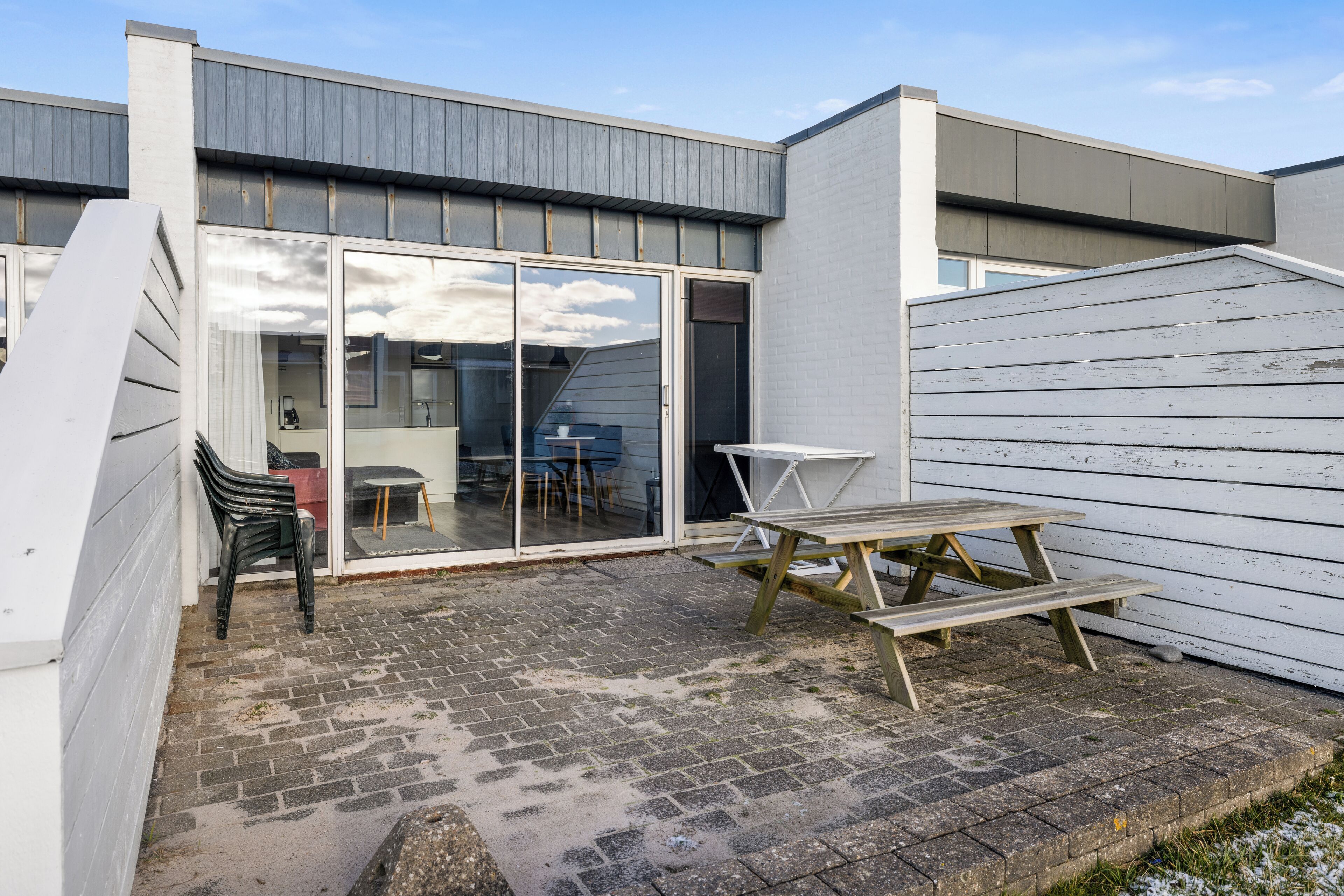 A patio area with a picnic table and chairs, a glass door entrance, and a brick floor.