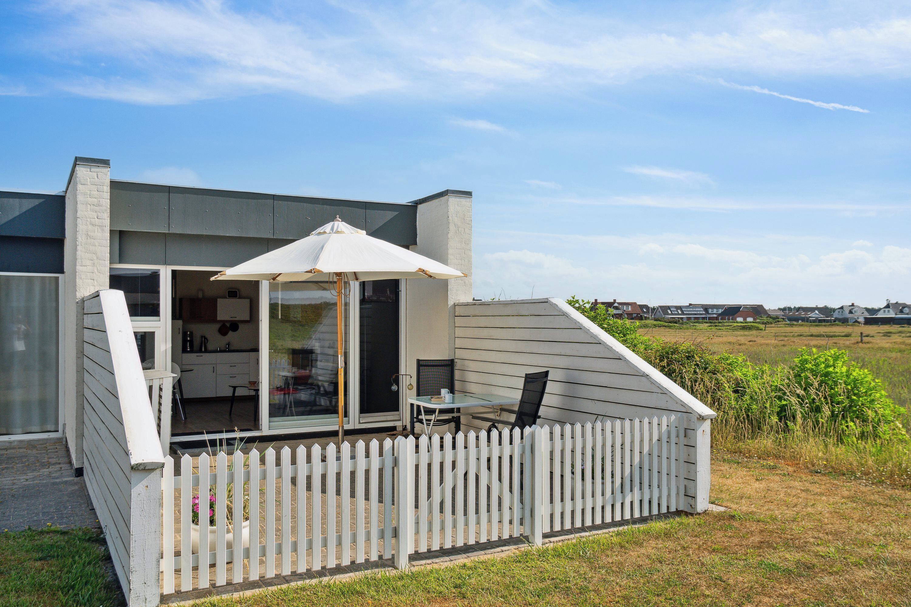 Una casa moderna con un patio cubierto, un comedor y una cocina visibles a través de puertas de cristal.