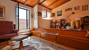 A cozy room with a wooden ceiling, a large window, a red chair, a wooden desk, a bookshelf, and a patterned rug. - Palace Andreis - Five Bedroom Holiday Home (Trogir)