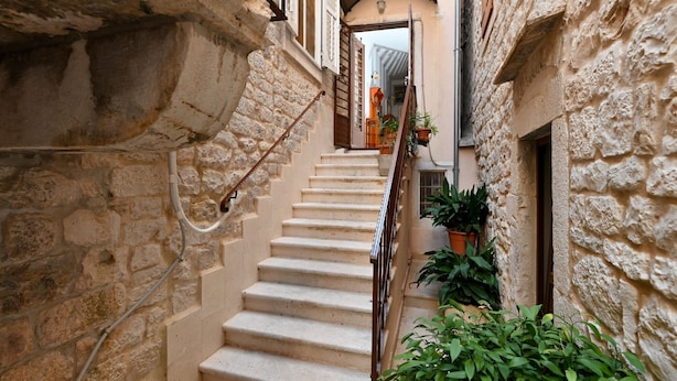 A narrow stone staircase with a metal railing, flanked by buildings with balconies and potted plants. - Palace Andreis - Five Bedroom Holiday Home (Trogir)