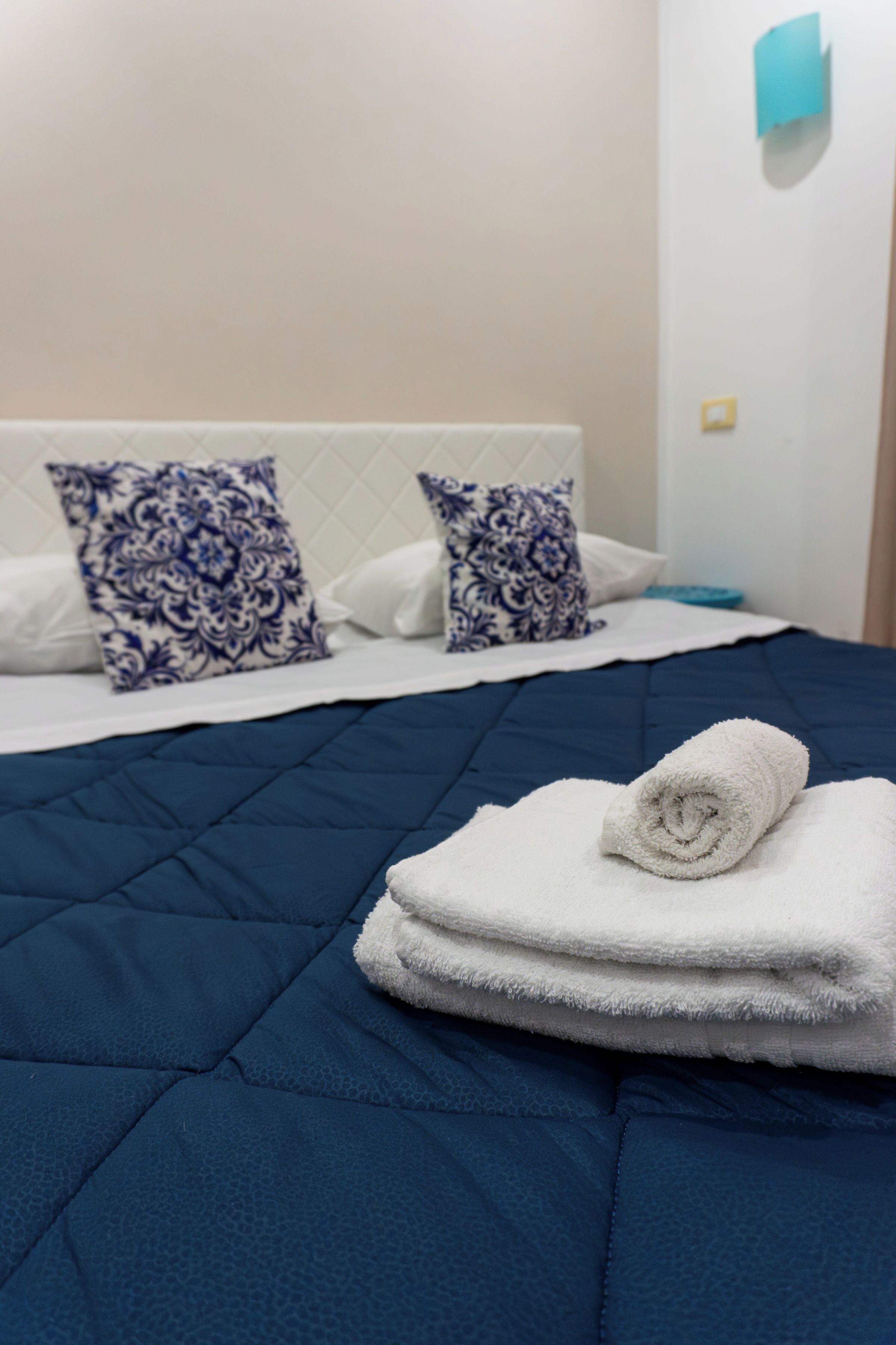 Een opgemaakt bed met een blauwe quilt, witte kussens en een gevouwen witte handdoek.
