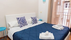 Un lit bien fait, avec une couette bleue, des oreillers blancs et des coussins à motifs bleus. Des serviettes blanches pliées sont posées sur le lit.