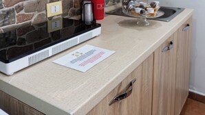 Une cuisine avec un pare-feu en pierre, une hotte de cuisinière en acier inoxydable, un évier et un plan de travail sur lequel se trouvent un grille-pain et un récipient rouge contenant des ustensiles.