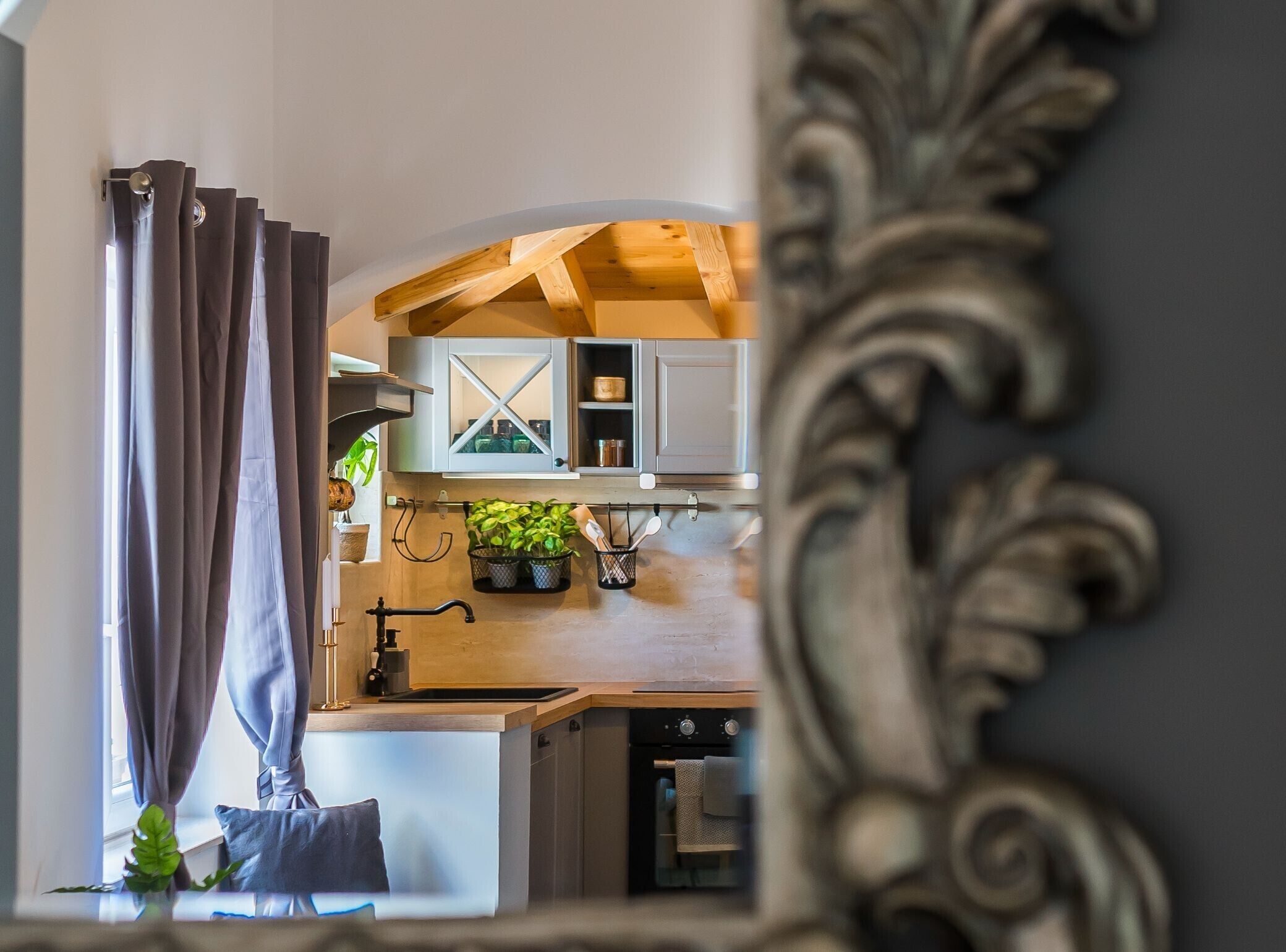A modern kitchen with wooden beams, a built-in oven, and a window with curtains.