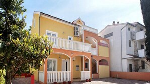 Un edificio de dos pisos con fachada amarilla, balcones blancos y un patio empedrado con ladrillos.
