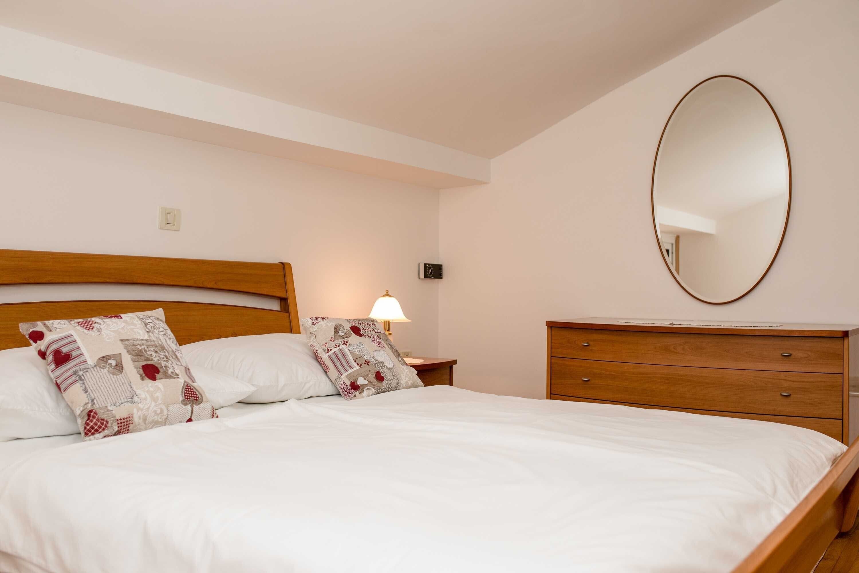 A neatly made bed with a wooden headboard, a bedside lamp, and a mirror on the wall.