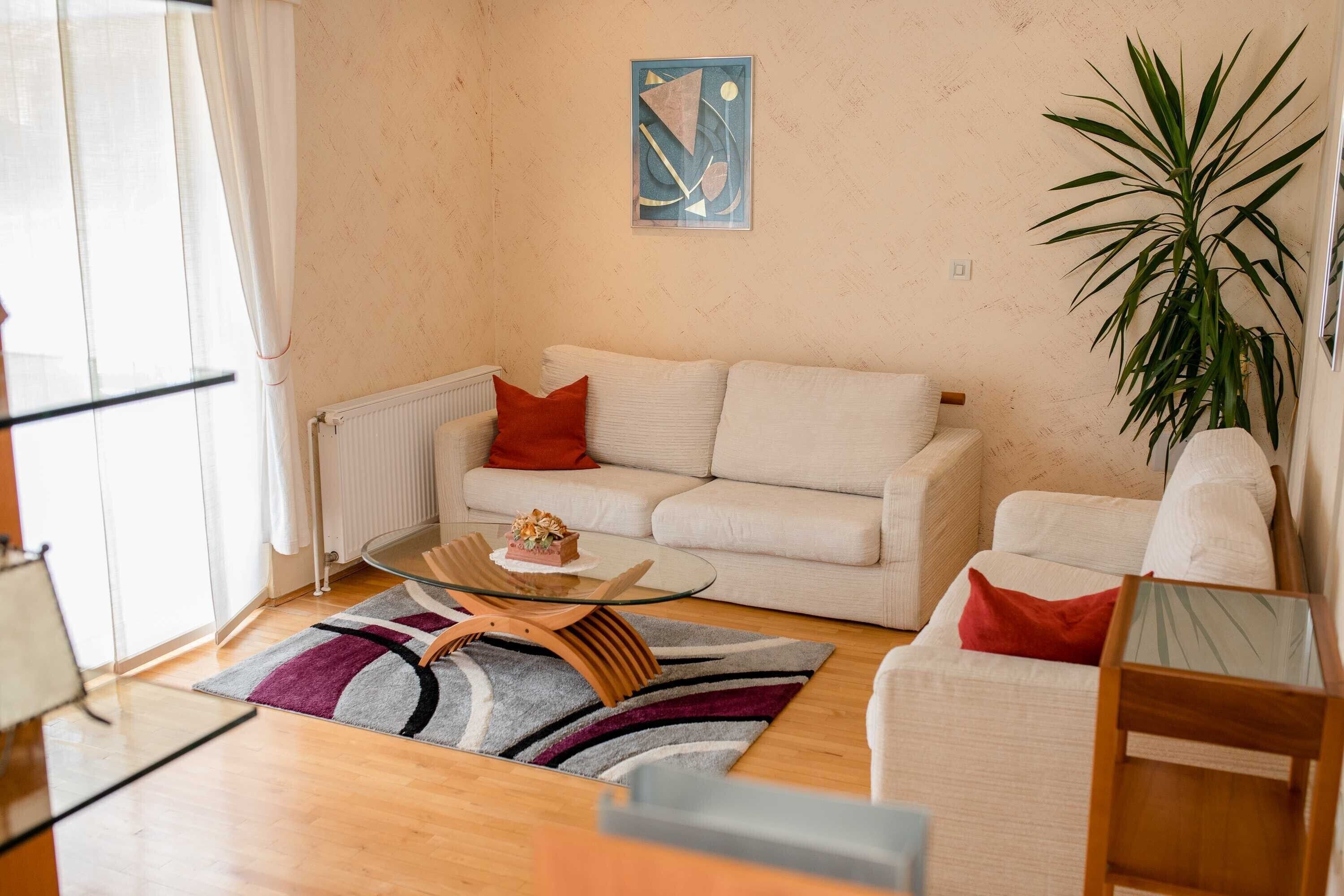 A modern living room with a white sofa, a glass coffee table, and a large potted plant.