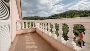 A balcony with a white balustrade, a tiled floor, and a view of a green hillside.