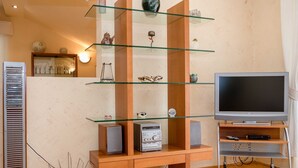 A modern living room with a glass shelf unit, a flat-screen TV, and a built-in sound system.
