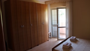 A bedroom with a wooden wardrobe, a bed with towels, and a sliding glass door leading to a balcony.