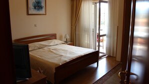 Une chambre à coucher avec un lit, une table de chevet, une lampe, un téléviseur et une fenêtre avec des rideaux.