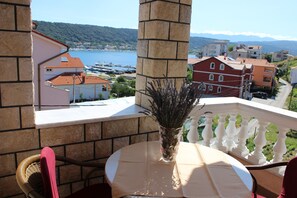 A balcony with a table and chairs, overlooking a coastal town with buildings and a body of water.