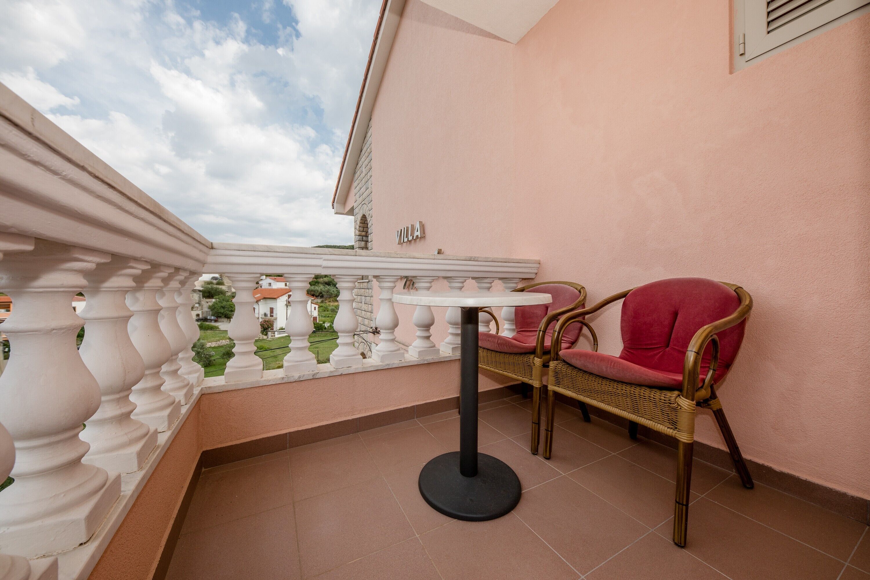 A balcony with a white balustrade, a wicker chair with a red cushion, and a round table.