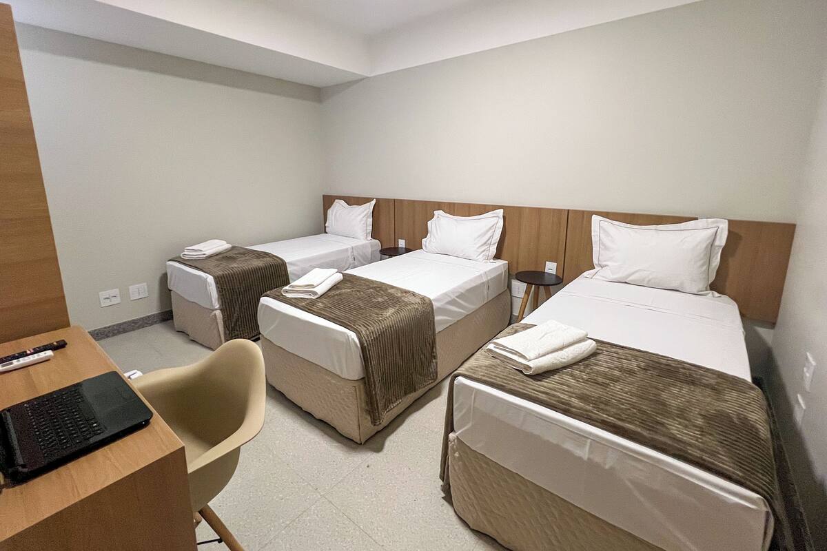 A hotel room with three single beds, a desk with a laptop, and a chair.