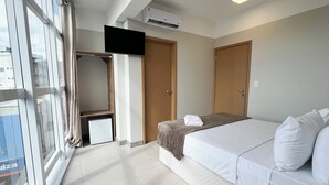Hotellihuone, jossa on sänky, televisio, vaatekaappi ja ikkuna, jossa on verhot.