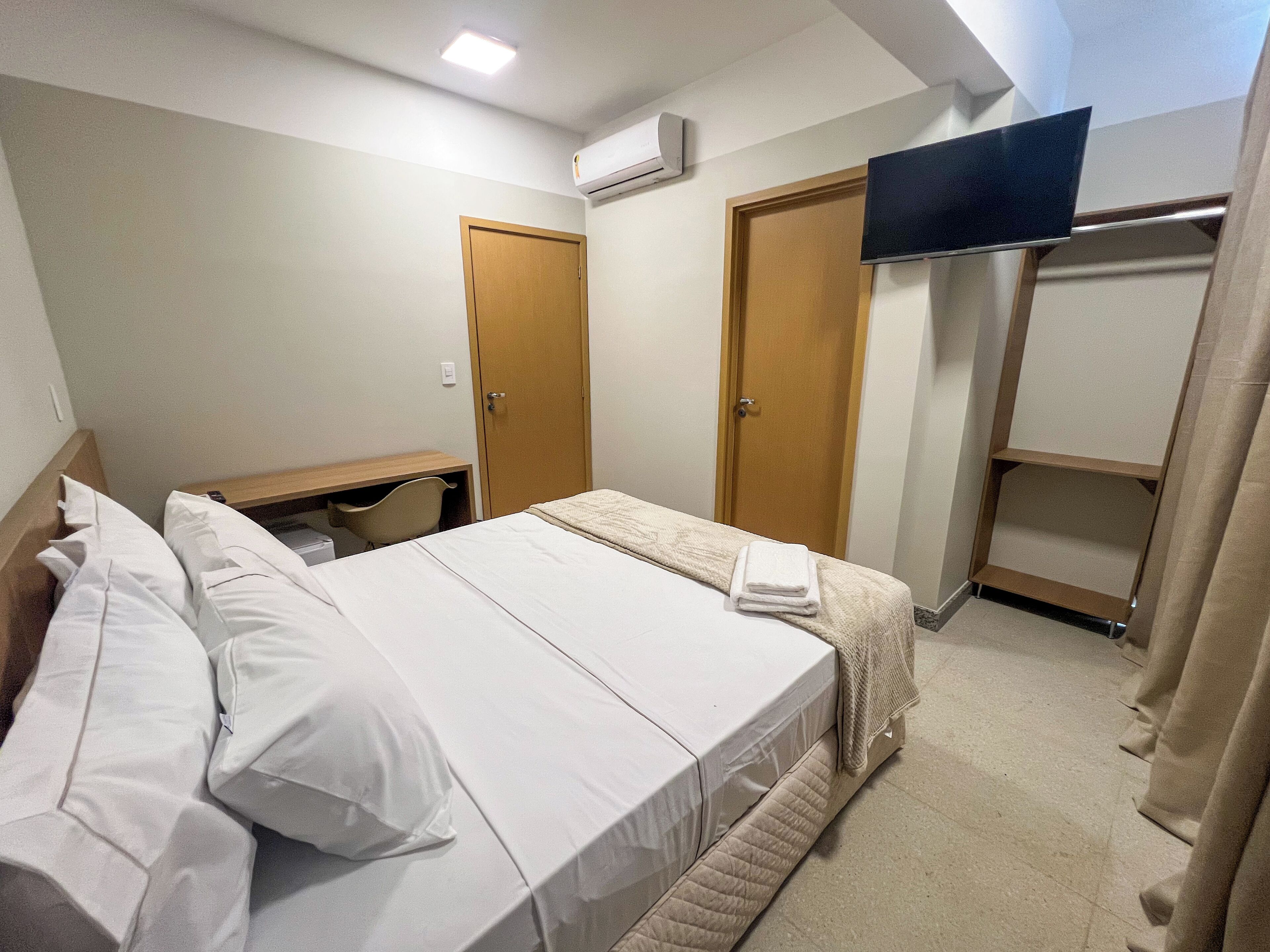 Una habitación de hotel con cama, escritorio, televisión montada en la pared y armario.