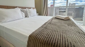 Hotellihuone, jossa on suuri sänky, ikkunasta avautuva näkymä taivaalle ja parveke, jossa on kaide.