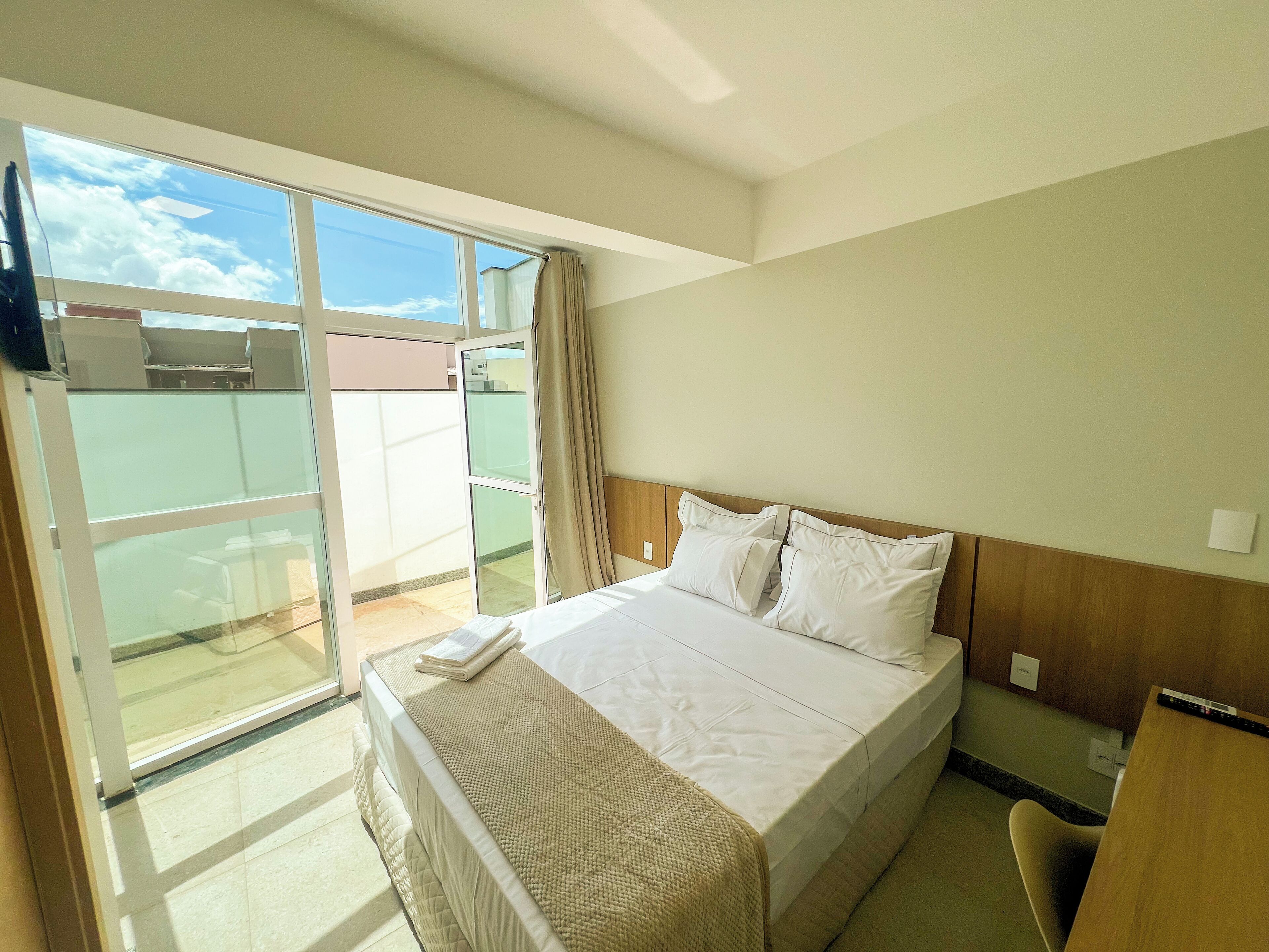A hotel room with a bed, a desk, and a view of the outside.