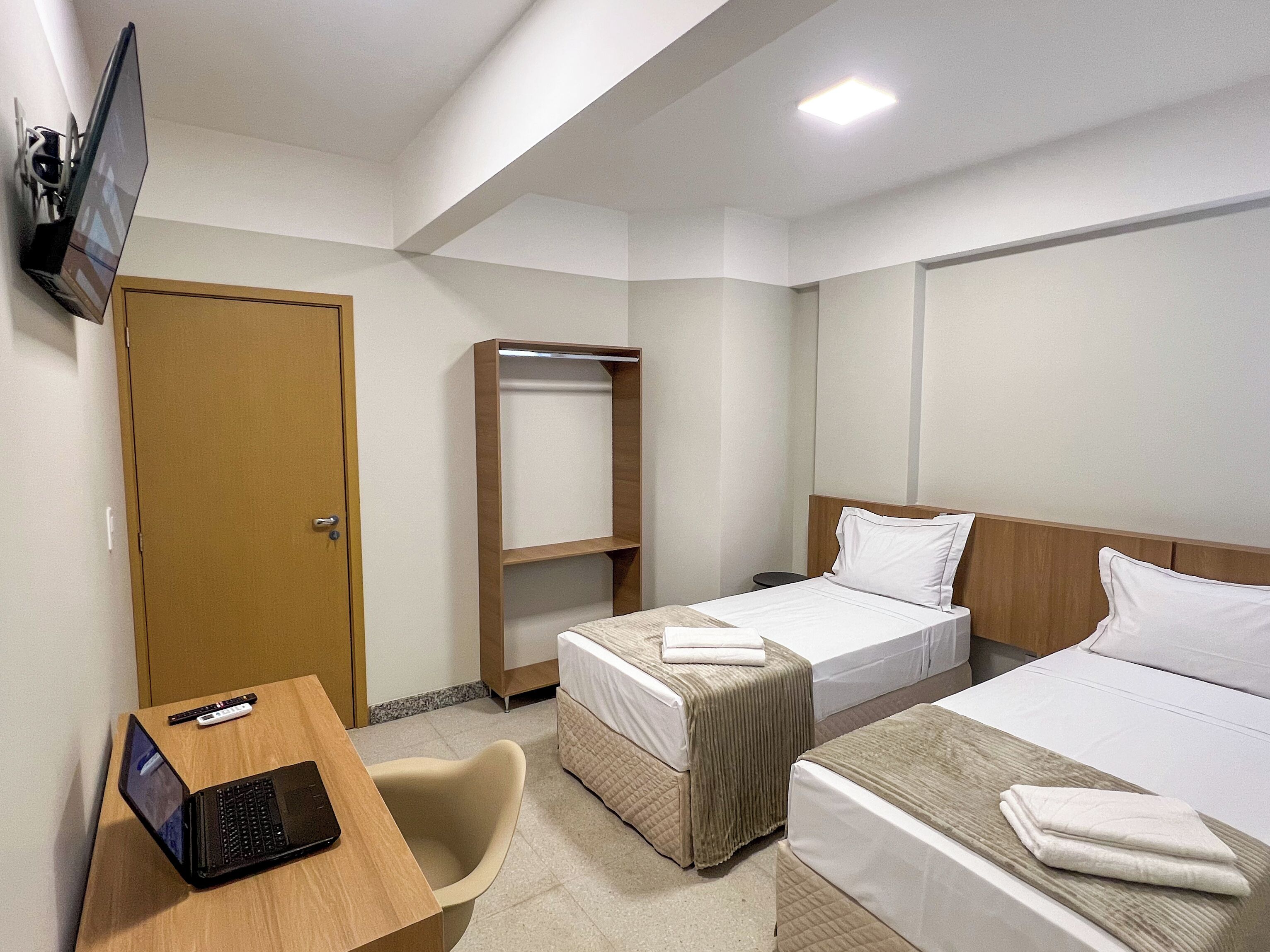 Habitación de hotel con dos camas, un escritorio con una computadora portátil, un televisor en la pared y un armario.