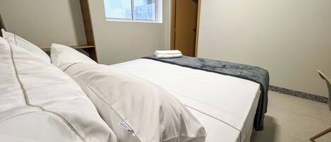 A hotel room with a bed, a window, an air conditioning unit, and a door.