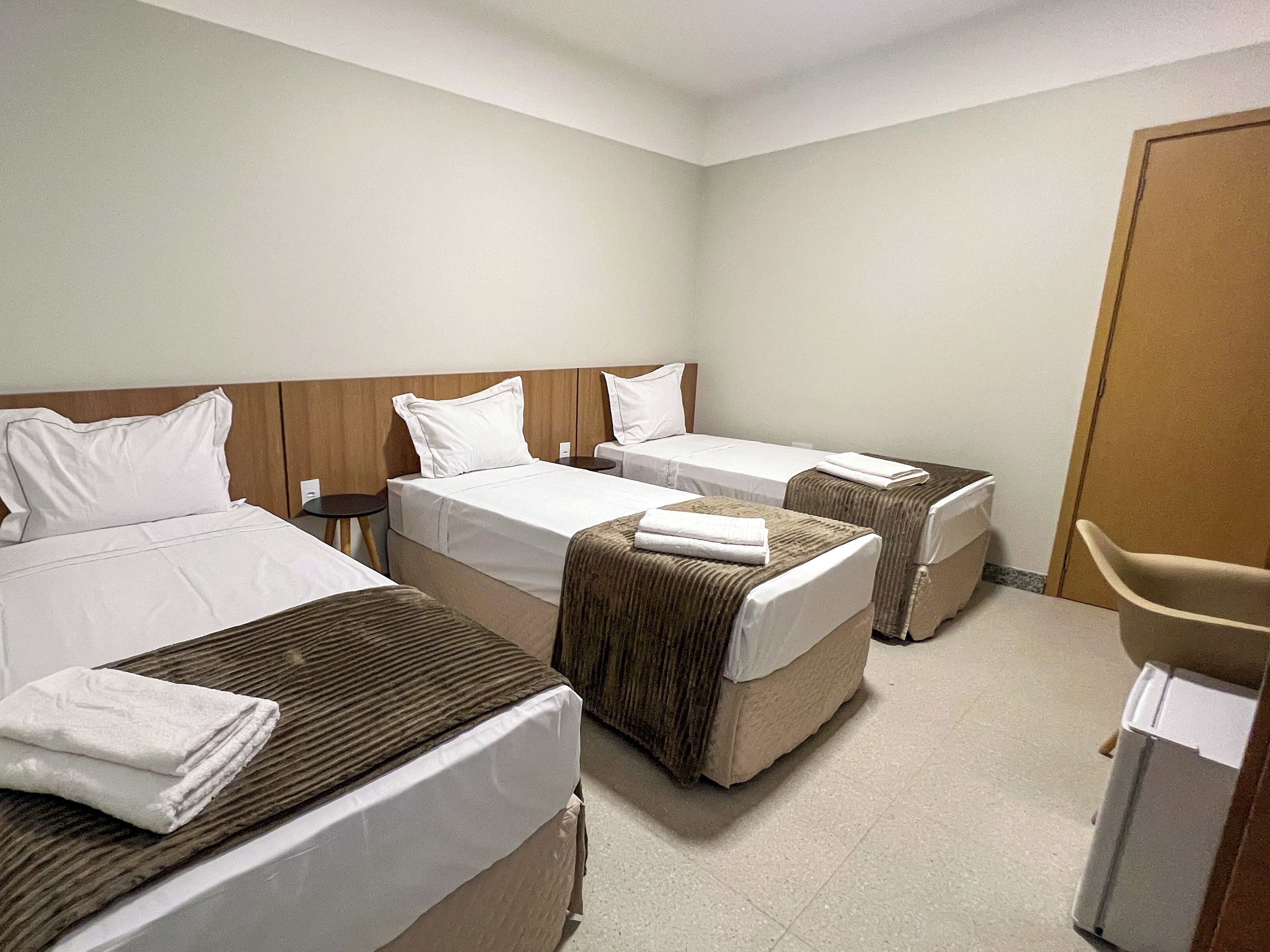 A hotel room with two single beds, a small table, and a chair.