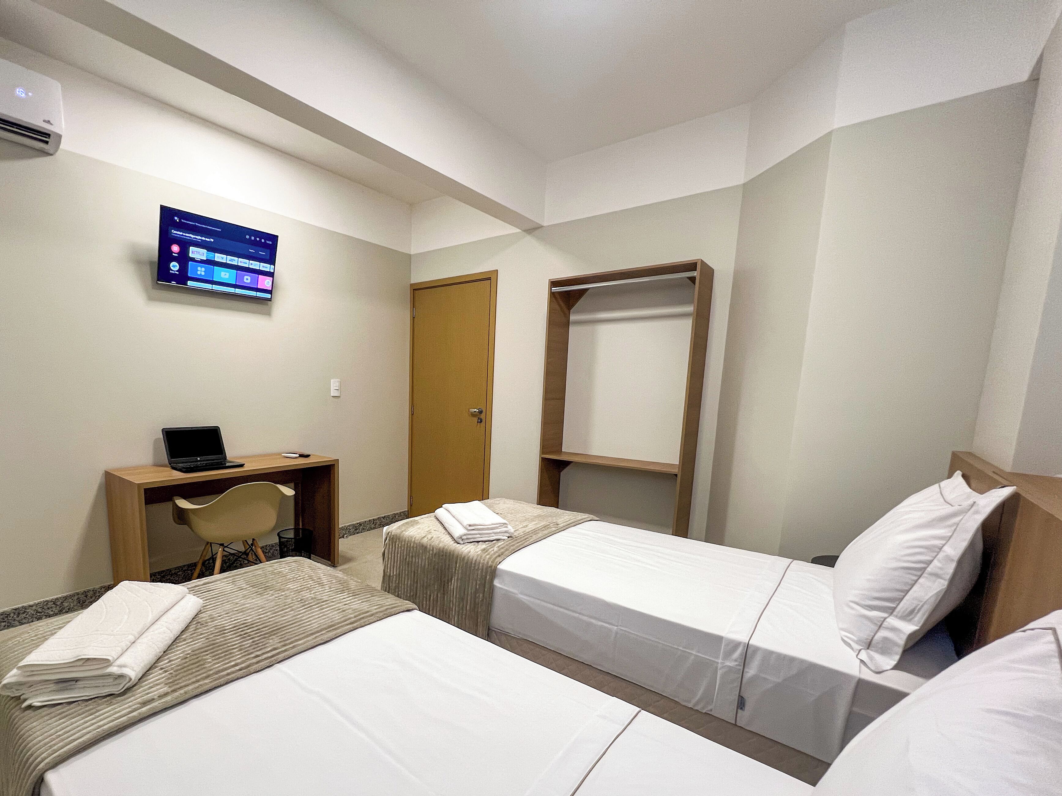 Habitación de hotel con dos camas, un escritorio, una silla, un televisor y un armario.