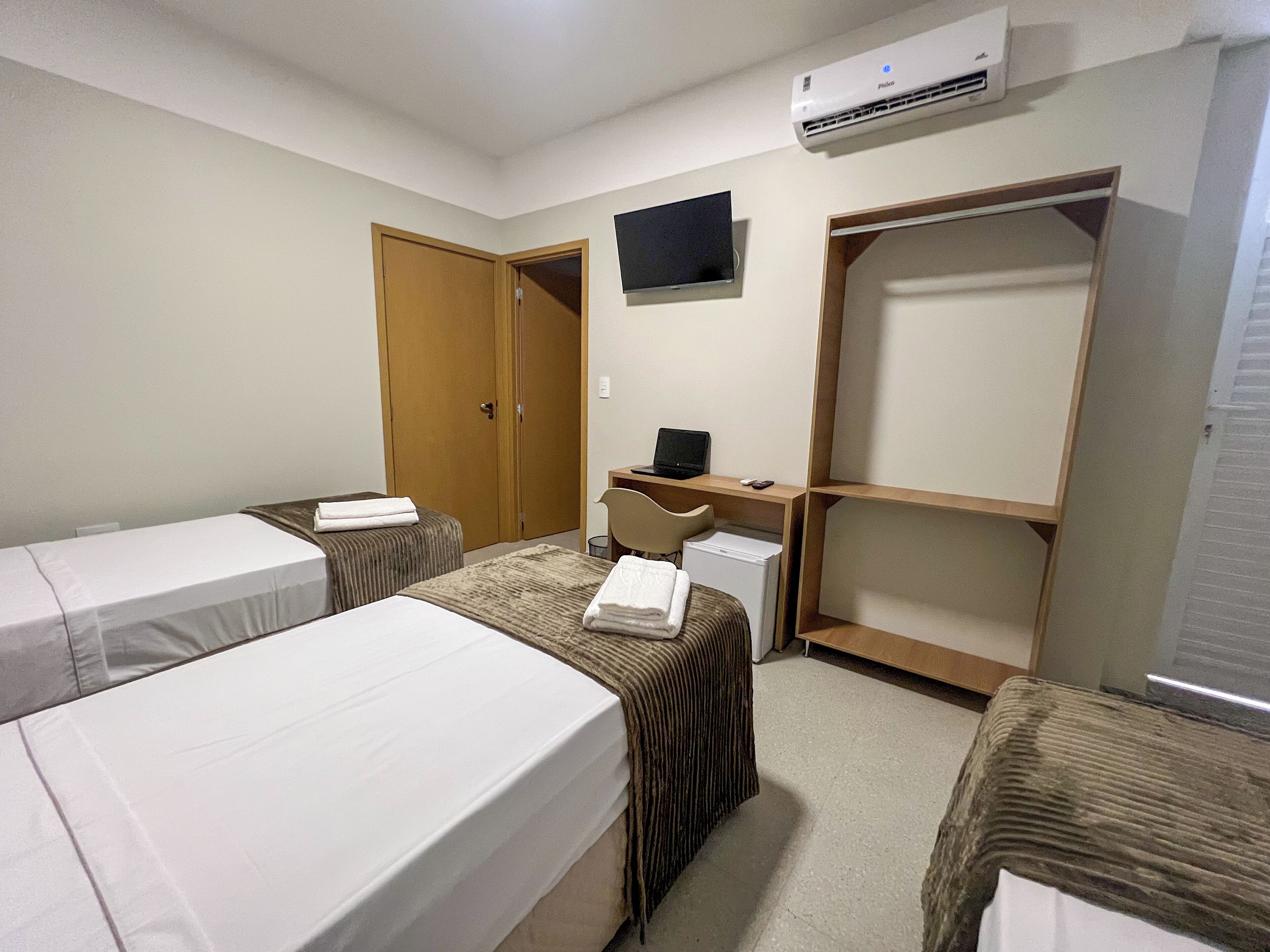 A hotel room with two beds, a desk with a computer, a TV, and a wardrobe.