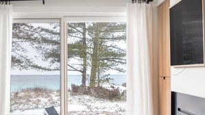 A bedroom with a bed, a TV, a fireplace, and a view of the beach.