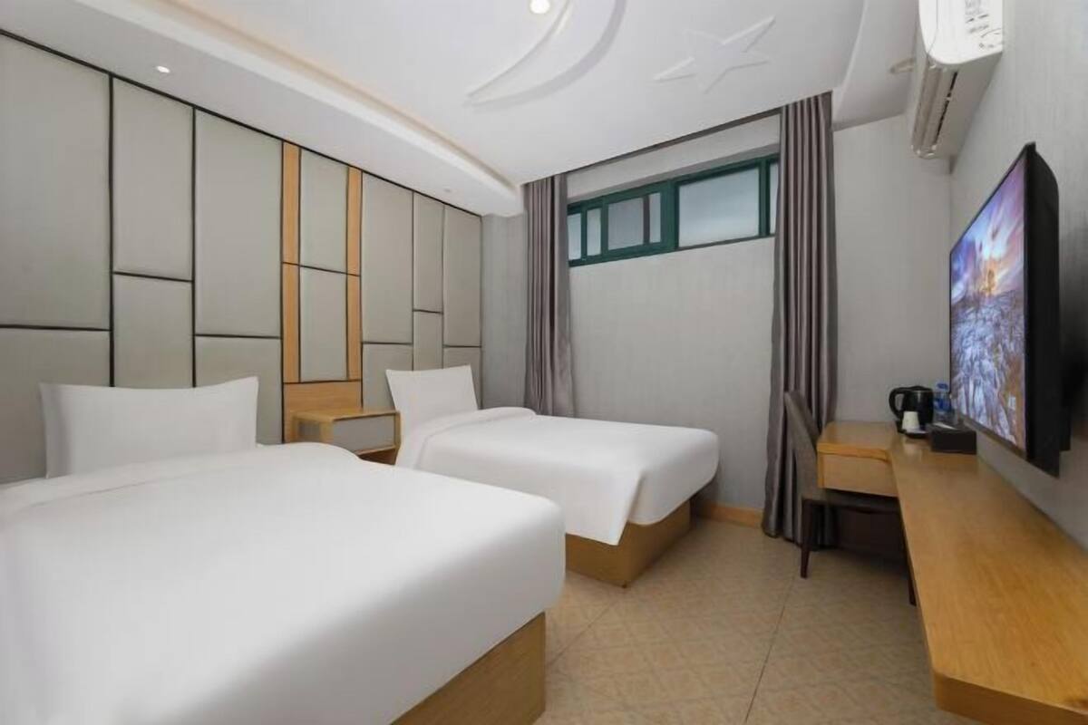 A hotel room with two beds, a desk, a TV, and a window with curtains.