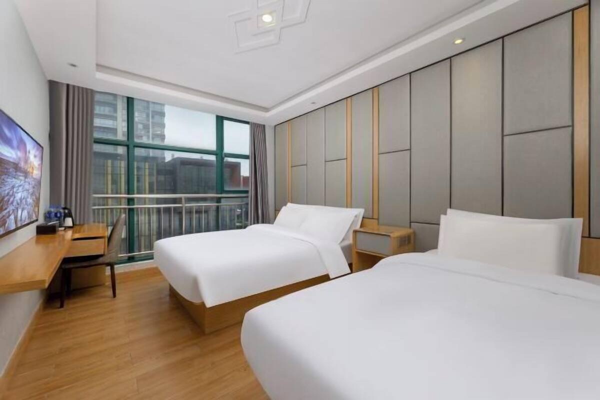 A hotel room with two beds, a desk, and a large window.
