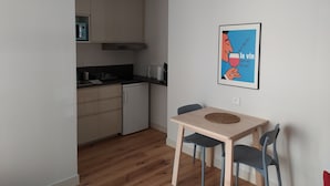 Kompakti keittiö, jossa on ruokailutila. Tilaan kuuluu pöytä ja kaksi tuolia sekä seinälle kiinnitetty juliste.
