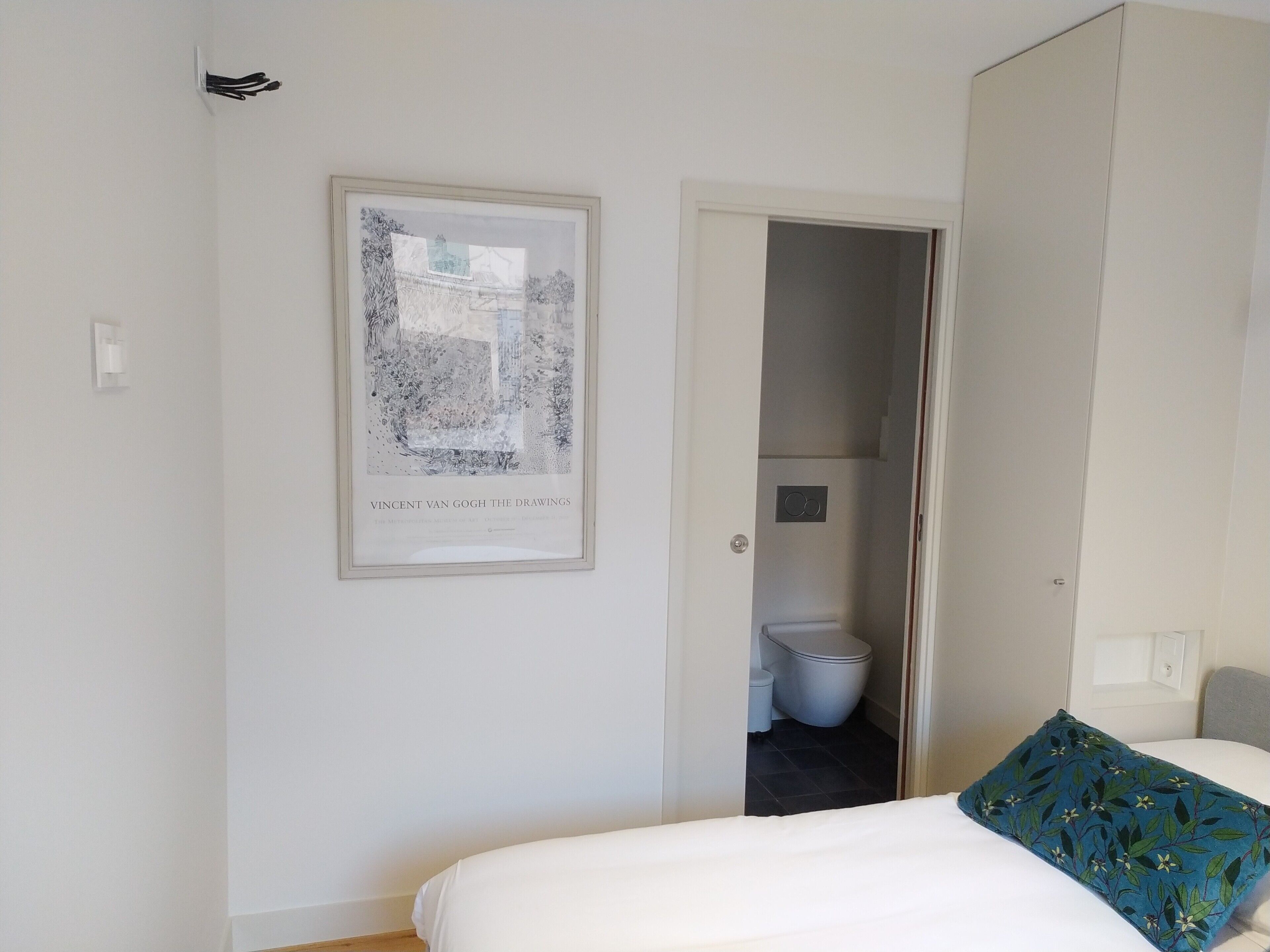 A bedroom with a bed, a framed artwork on the wall, and a view into the bathroom.