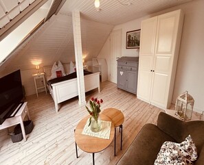 Une pièce de style « loft » avec un plafond en pente, une télévision, un canapé, une petite table avec un vase et une armoire.
