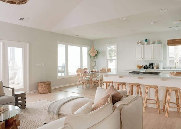 A spacious living area with a large sofa, a dining table, and a kitchen area with white cabinets and a bar stool.